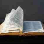 An open book with pages turning, reminiscent of the tales of the sons of Adam and Eve in the Bible, set against a dark background.