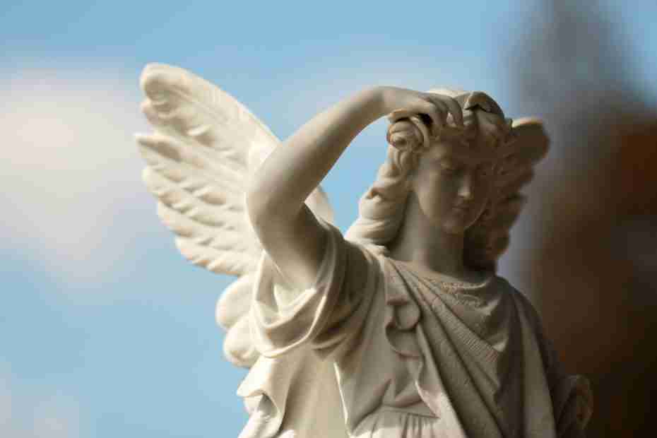 Um close-up de uma estátua de anjo de pedra branca com asas e uma expressão serena, em um céu azul com nuvens claras, evoca imagens dos Filhos de Deus na Bíblia.