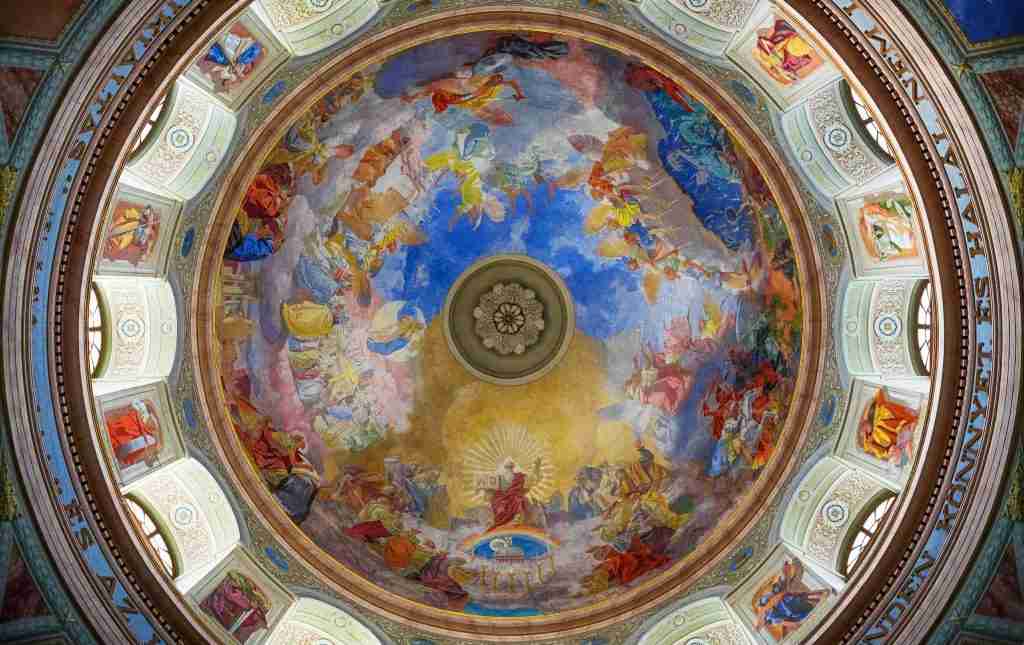 Un fresco vibrante y colorido que representa diversas escenas históricas y bíblicas, incluidos los Hijos de Dios de la Biblia, adorna el interior de un gran techo abovedado.
