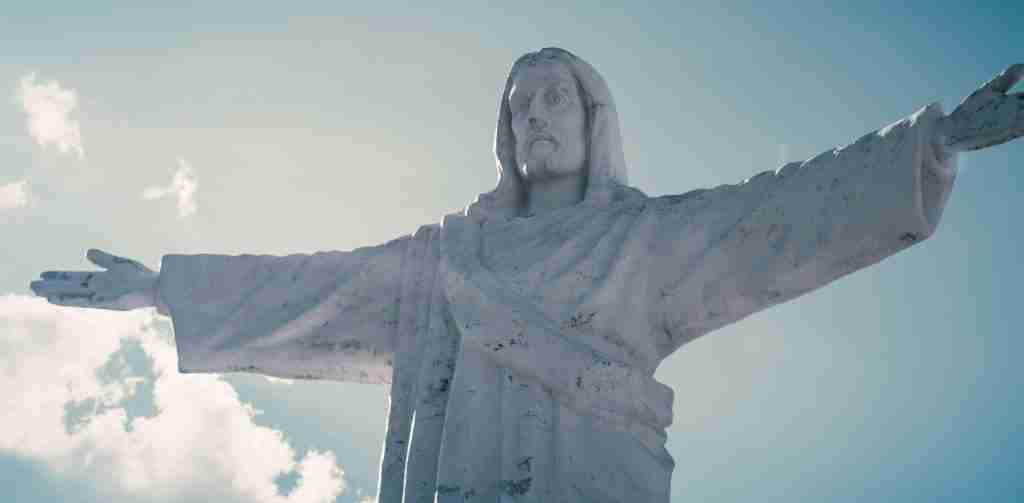 Una imponente estatua blanca de Jesucristo con los brazos extendidos sobre un fondo de cielo nublado, que encarna la gracia y el poder de los Hijos de Dios de la Biblia.