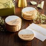 Marble and wood coasters with personalized engravings, surrounded by flowers, a gift box, and a congratulations card make thoughtful baptism giveaway ideas.