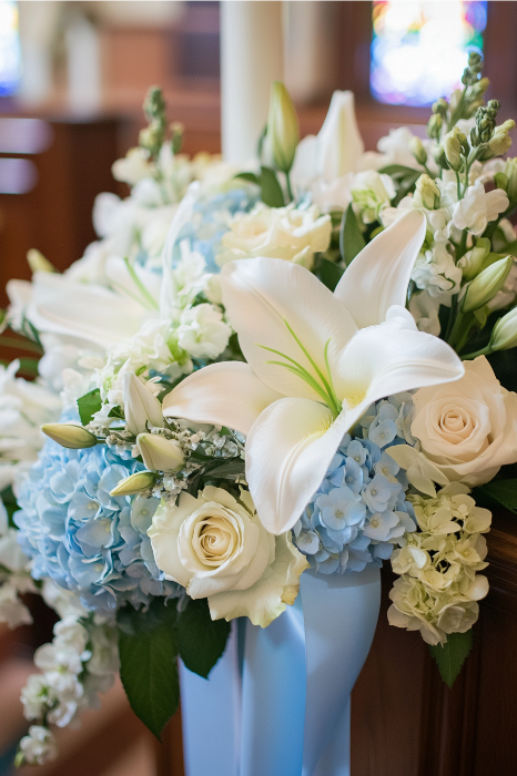 Un precioso arreglo floral para altares de iglesias, este ramo presenta lirios blancos, rosas y hortensias azules, elegantemente acentuados con una cinta azul claro.