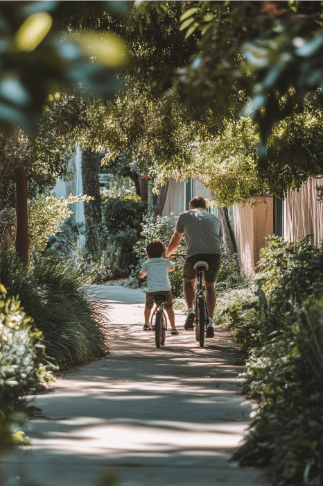 Un adulto y un niño comparten un alegre paseo en bicicleta por un sendero iluminado por el sol, rodeados de exuberante vegetación, encarnando el espíritu de unión que se encuentra en los poemas del Día del Padre para la iglesia.