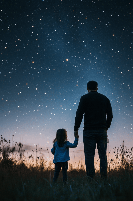 Un niño y un adulto se cogen de la mano mientras contemplan un cielo lleno de estrellas en un campo abierto, y su vínculo se hace eco de la calidez que a menudo se celebra en los poemas del Día del Padre para las reuniones eclesiásticas.