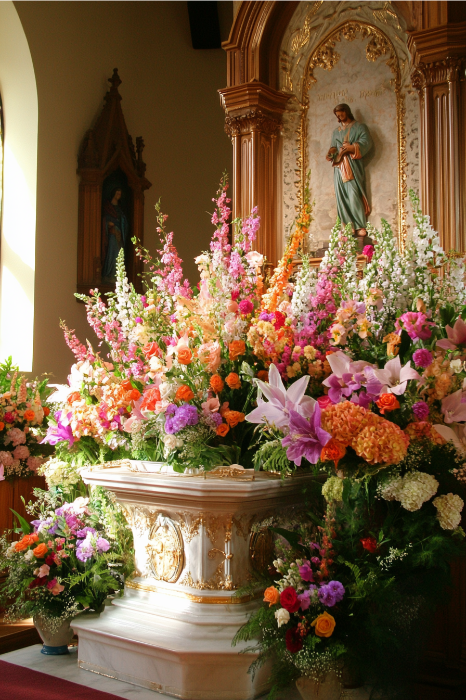 Un altar de iglesia adornado con vibrantes ideas de arreglos florales para altares de iglesia y una estatua religiosa al fondo.