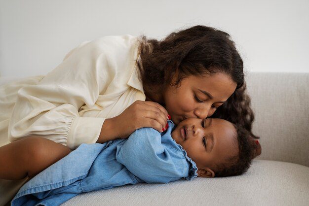 Nestled on a cozy couch, the scene evokes the cherished bond reminiscent of Noah's wife in the Bible nurturing instinct, as a mother lovingly kisses her baby's forehead.