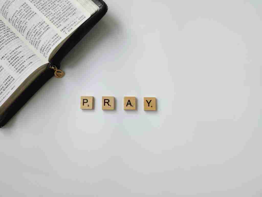 Una Biblia abierta y fichas de Scrabble con la palabra "PRAY" dispuestas sobre una superficie blanca, que reflejan la importancia de las oraciones diarias por AA.