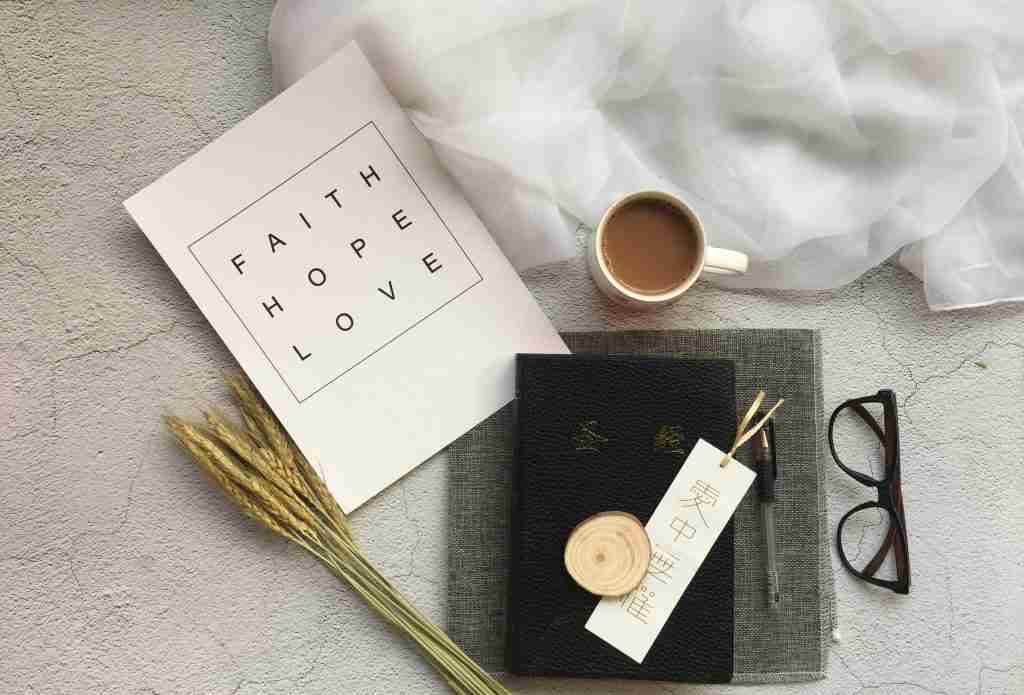 Un diseño plano con libros, una taza de café, vasos y trigo rodea una tarjeta "Faith Hope Love" sobre una superficie texturizada que recuerda escenas de la escuela dominical.