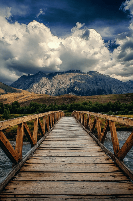 Un puente de madera que conduce hacia las montañas bajo un cielo nublado ofrece un camino tranquilo, que invita a pensar y a rezar en silencio por la ansiedad en medio del abrazo sereno de la naturaleza.
