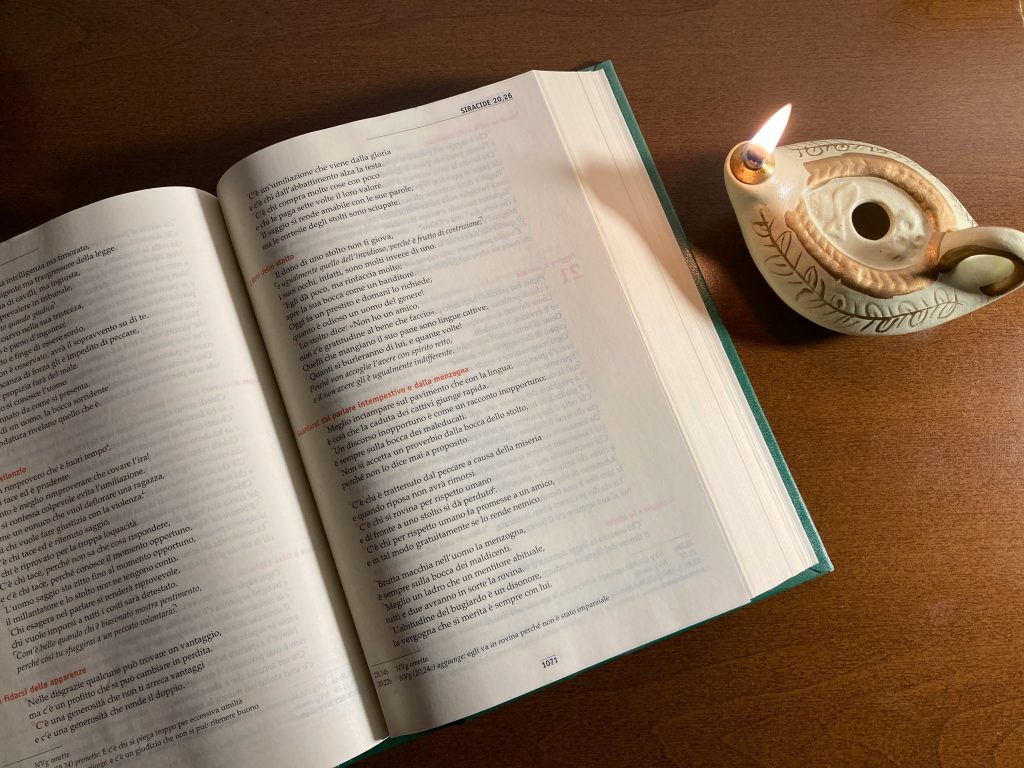 A Bible lays open with a candle next to it on a table, showing fire in the Bible