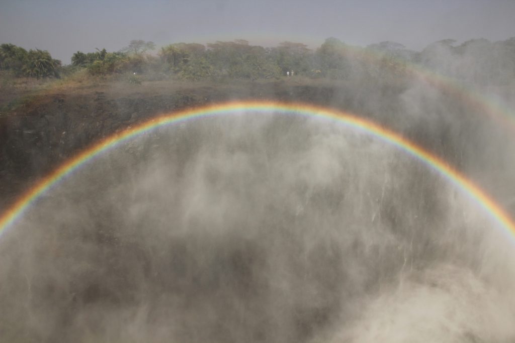 A rainbow arches over misty waterfalls, a scene reminiscent of the biblical symbol found in lush greenery.