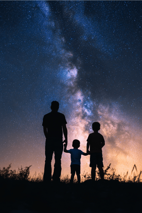 Bajo el cielo estrellado de la noche, un padre y sus dos hijos contemplan asombrados las estrellas, celebrando su unión como en los versos de los queridos poemas del Día del Padre para la iglesia, con la Vía Láctea como telón de fondo.