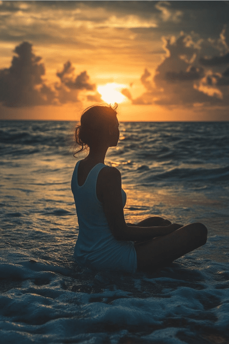 La silueta de una persona sentada junto al mar durante la puesta de sol, reflexionando sobre la oración AA por la ansiedad mientras las nubes pasan a la deriva y las suaves olas bañan la orilla.