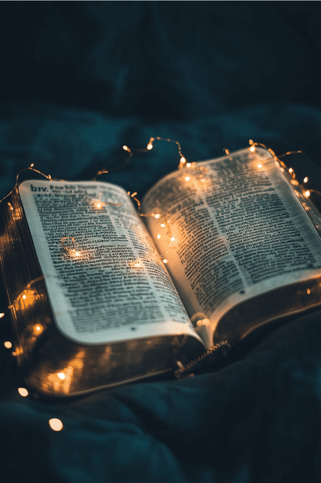 Un libro abierto de poemas para la iglesia está rodeado de cálidas y brillantes luces de hadas en un entorno oscuro.