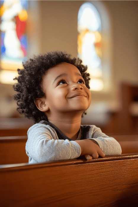 Un niño resplandece de alegría, mirando hacia arriba mientras está acurrucado en un banco de la iglesia. Las vibrantes tonalidades de las vidrieras difuminadas bailan detrás, haciéndose eco del espíritu que se respira en las reuniones de la iglesia de los niños.