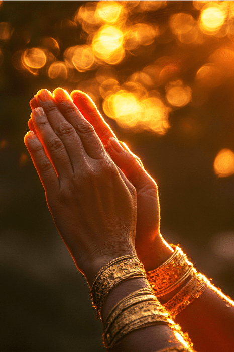 Manos en oración con brazaletes dorados contra una puesta de sol resplandeciente y suavemente enfocada, que recuerda la reflexión pacífica que se encuentra en la Oración de Gratitud de AA.
