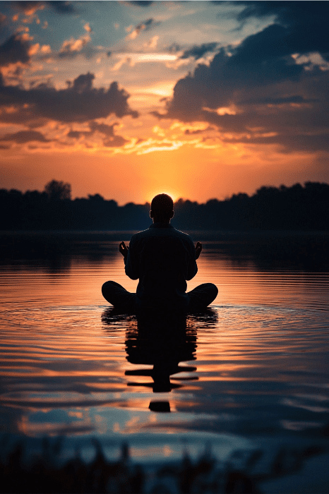Mientras el sol se pone sobre el tranquilo lago, pintando el cielo con vibrantes reflejos naranjas y azules, una persona medita apaciblemente, encarnando un sentimiento de gratitud que recuerda a la Oración de Gratitud de AA.