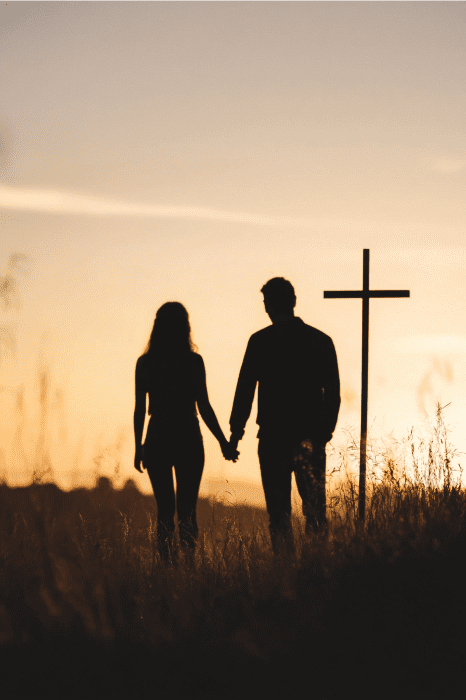 Silhouetted couple holding hands at sunset near a cross in a field, an image reminiscent of KJV Devotions for Married Couples.