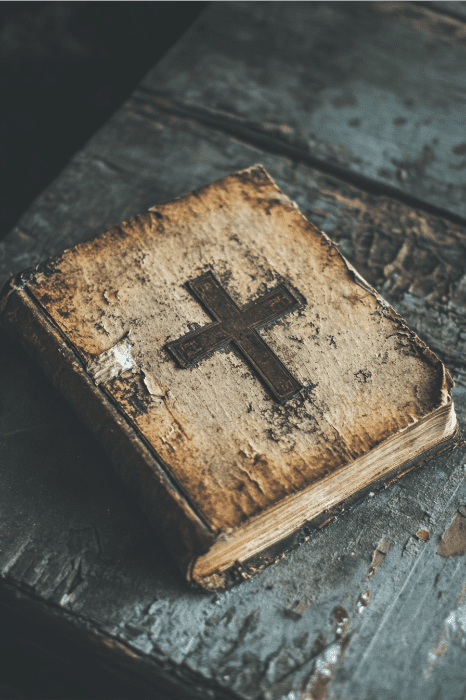 Um livro antigo e desgastado intitulado "Scriptures for Unity in the Church" (Escrituras para a unidade na Igreja) repousa graciosamente em uma superfície de madeira desgastada, com a capa adornada com uma cruz sutil.