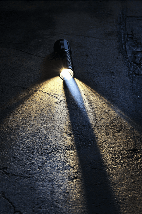 Uma lanterna, que lembra o Object Lessons for Church, lança um amplo feixe de luz em uma superfície escura e texturizada.