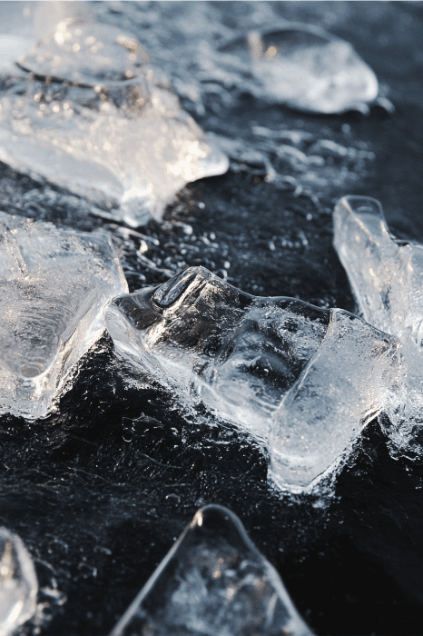 Primer plano de trozos de hielo derritiéndose sobre una superficie oscura y húmeda, evocando la fluidez y la innovación que se encuentran en las ideas creativas de los servicios a la juventud.
