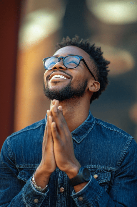 Pessoa de camisa jeans e óculos, sorrindo com as mãos juntas, olhando para cima, aparentemente inspirada por ideias de História Negra para a igreja.