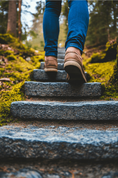 Una persona en vaqueros y botas sube por unos escalones de piedra musgosa en un bosque, reflexionando sobre ideas innovadoras para la captación de fieles.