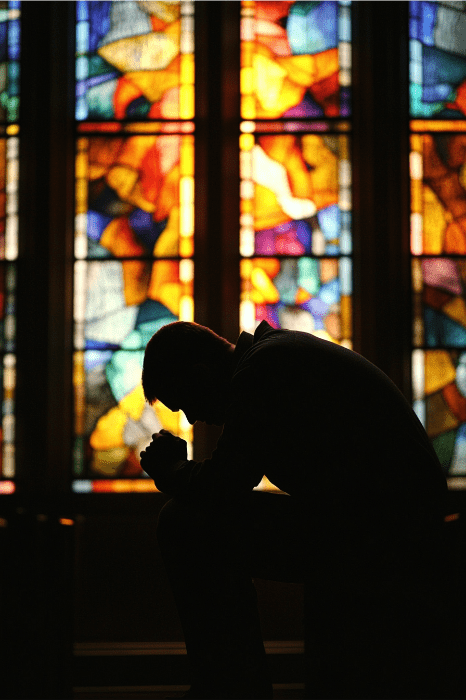Silhouette of person engaged in a prayer for church growth, standing before vibrant stained glass windows.
