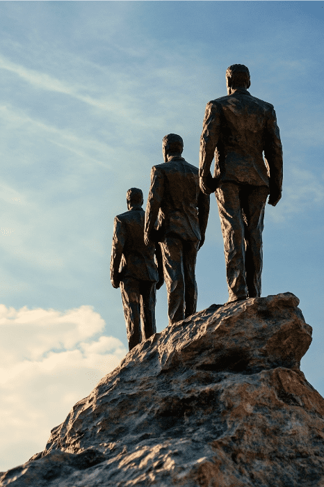 Las estatuas de bronce de tres hombres trajeados se yerguen sobre una colina rocosa, encarnando la fuerza y la visión propias de los planes estratégicos de las iglesias, mientras miran resueltamente hacia la infinita extensión de un cielo azul.