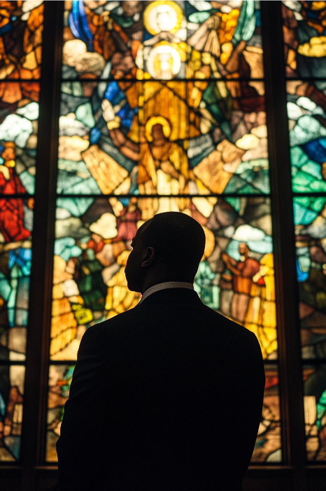 Silhueta de um homem em frente a um vitral vibrante em um ambiente de igreja, evocando ideias poderosas da História Negra por meio de sua variedade de cores.