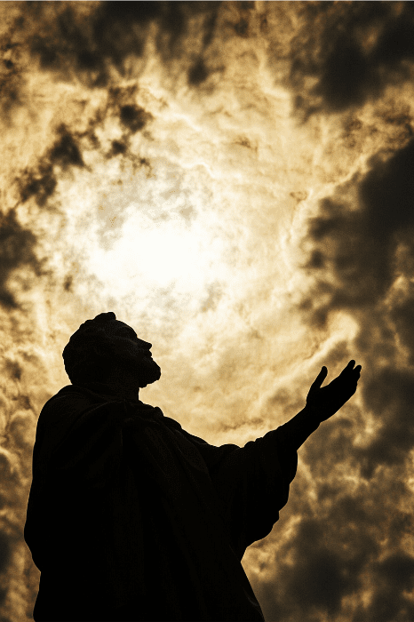 La silueta de una estatua con el brazo extendido contra un cielo nublado y dramático recuerda a los signos de la Biblia, mientras la luz del sol se abre paso.