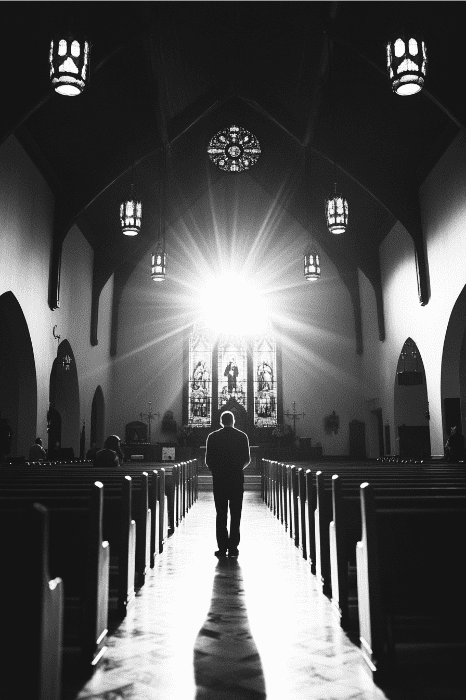 Una persona de pie en el pasillo de una iglesia, a contraluz de la luz del sol que se cuela por las vidrieras, evoca la poderosa imaginería del comentario de Hechos 3.