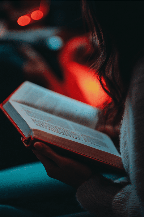 Una persona se sumerge en un libro de cubierta roja, suavemente iluminado por una cálida luz ambiental, que despierta en su mente ideas creativas de servicio a la juventud.