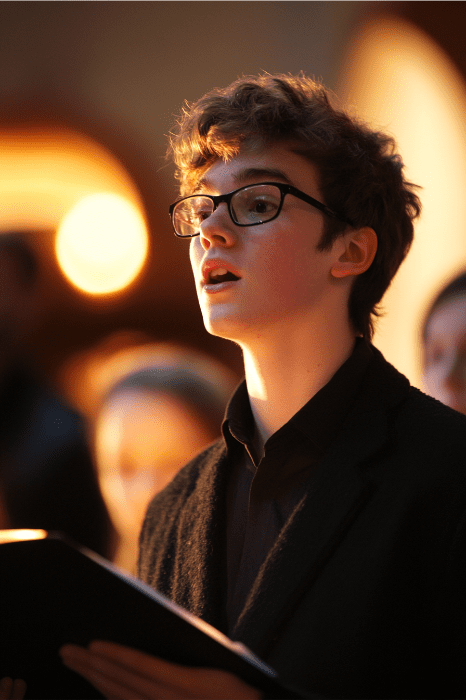 Em um ambiente de concerto bem iluminado, uma pessoa de óculos cativa o público cantando e segurando uma pasta de música, incorporando o espírito das ideias de programas de Natal para jovens da igreja.