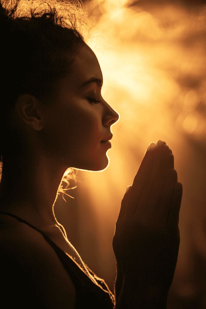 In a moment of serene reflection, the person in profile prays with closed eyes and hands together, as if finding solace through a mental health bible study. Warm light from behind gently illuminates their face, creating an aura of peace and introspection.
