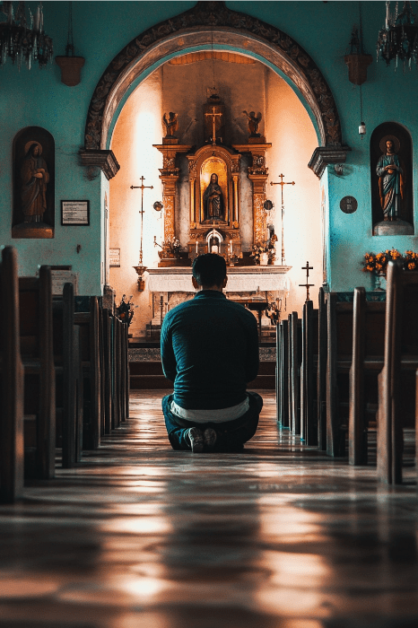 Una persona se arrodilla en oración en el interior de una iglesia, reflexionando sobre la pregunta "¿Cuáles son las oraciones de AA?". Su mirada está fija en el altar, donde las estatuas religiosas y una cruz están cálidamente iluminadas.