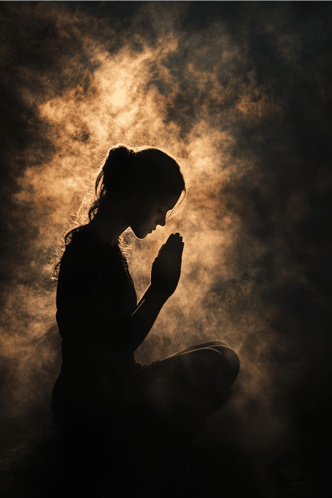 Silueta de una persona sentada en oración con las manos entrelazadas, rodeada de una iluminación espectacular y bruma, que evoca el espíritu sereno de las oraciones de Alcohólicos Anónimos.