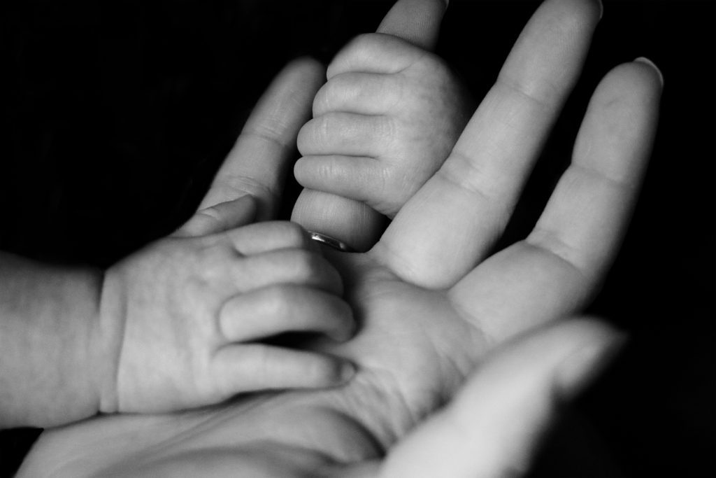 Close-up of a baby's hands gently holding an adult's hand in black and white, evoking the timeless compassion seen in stories of orphans in the Bible.
