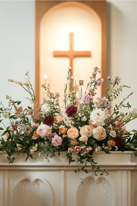 Cautivadoras ideas de arreglos florales para altares de iglesias que cobran vida con este despliegue floral, bellamente complementado con la cruz de madera del fondo.