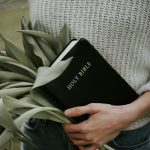 Flowers in the Bible - Meaning, Verses & Images A person gracefully holds a Bible and a bouquet of tulips, showcasing the beauty of flowers in the Bible, all while wrapped in a cozy knit sweater.