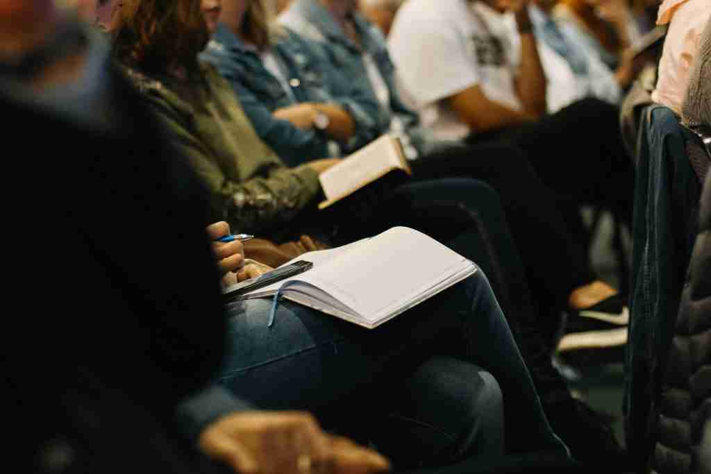 Las personas sentadas en una reunión o conferencia, tomando notas en cuadernos abiertos, se comprometen profundamente con la pregunta: ¿Cuáles son las oraciones de AA?