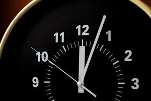 Un primer plano de un reloj negro muestra la hora: 11:59, con números y manecillas blancos, lo que quizá incite a reflexionar sobre los momentos que preceden a la medianoche y a plantearse significados como "¿Qué significa el número 6 en la Biblia?" en medio de su elegante diseño.