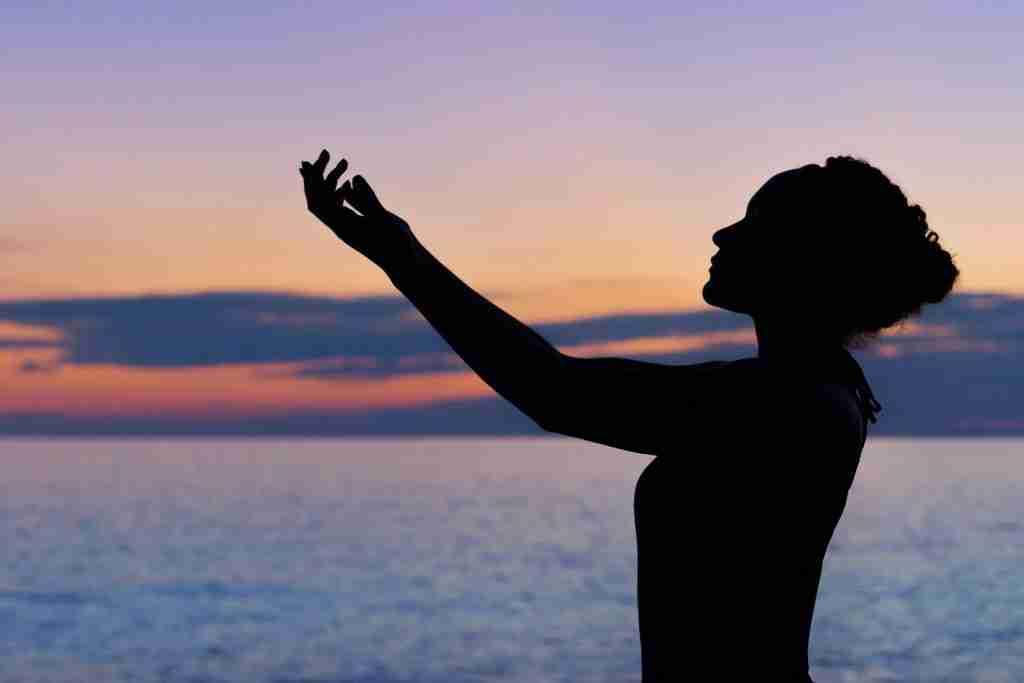 Silhouette of a person with raised hands against a sunset backdrop over the ocean, symbolizing daily prayers for AA.