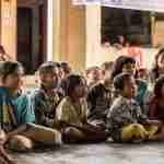 Children sit on the floor, smiling and looking forward in a classroom setting, captivated by the Esther Sunday School lesson.