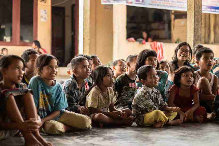 Los niños se sientan en el suelo, sonrientes y con la mirada fija en el aula, cautivados por la lección de la Escuela Dominical Esther.