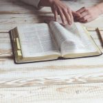 Una persona hojea un libro subrayado sobre una mesa de madera con un lápiz cerca, absorta en la historia de quién se casó con Rut en la Biblia.