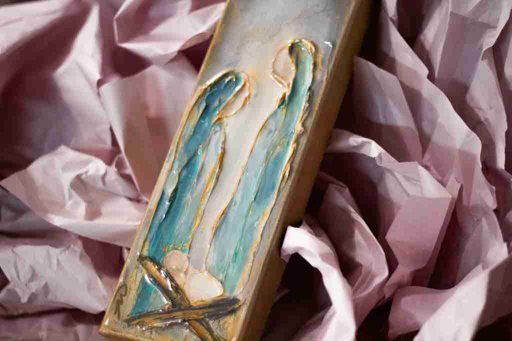 Uma obra de arte retangular que representa duas figuras abstratas e alongadas com detalhes em azul e dourado, aninhadas em papel rosa amassado, que lembra histórias bíblicas como a de José que se casou com Maria.