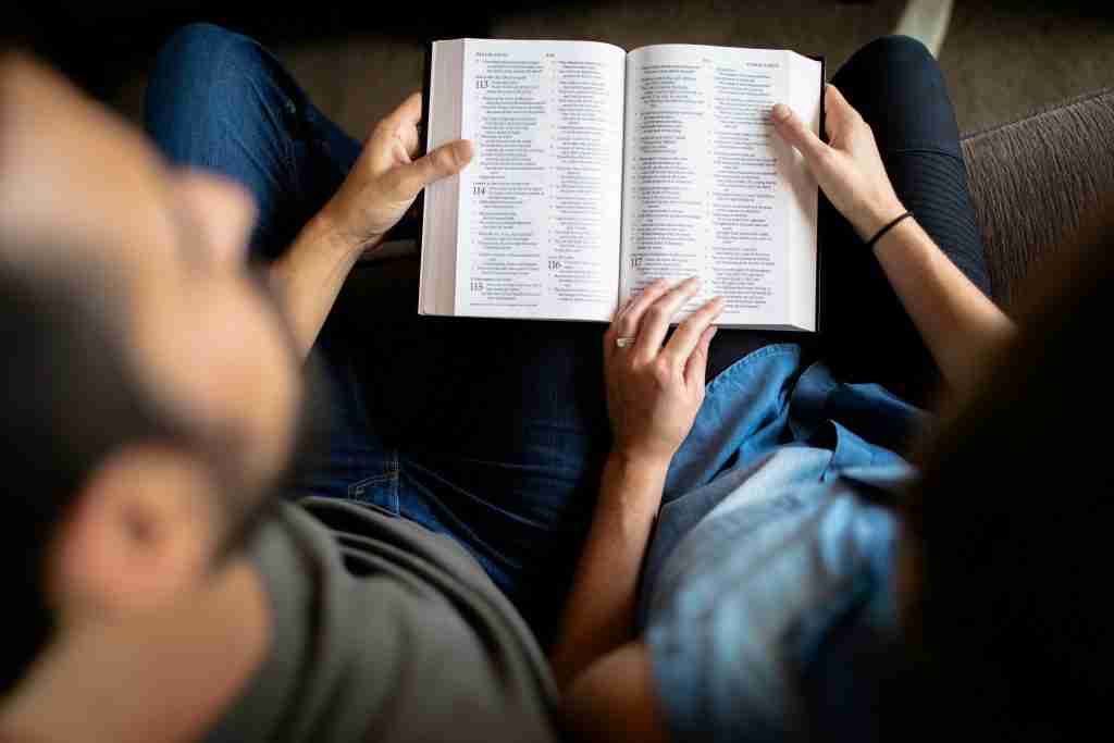 Two people sit closely, reading a book together, engrossed in the story of the Fisher of Men. One points at a page with blue text highlights, drawing attention to the meaningful passage.