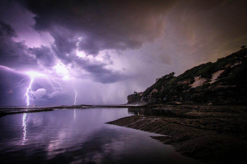 Una tormenta eléctrica azota el paisaje costero, las nubes oscuras se ciernen mientras el agua refleja la tempestad. Es como si la naturaleza canalizara el poder y el temor de los Hijos del Trueno de la Biblia.