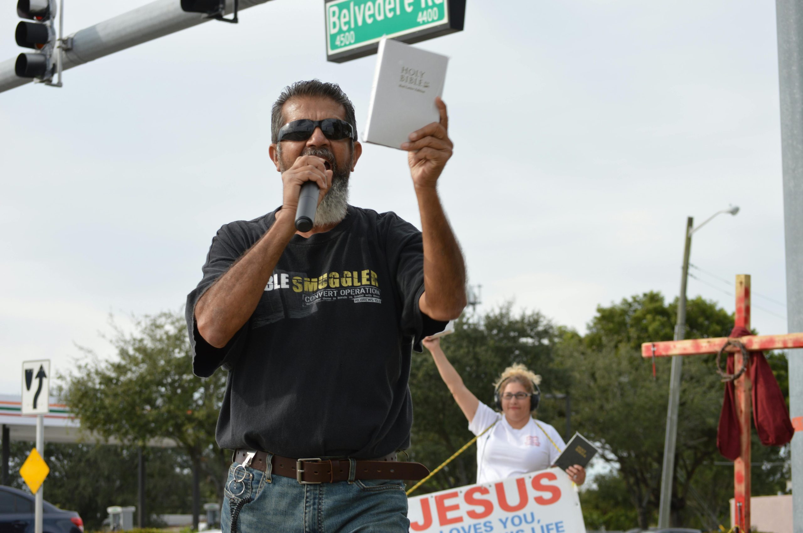 A man with a microphone holding a Bible and evangelizing on a street corner.